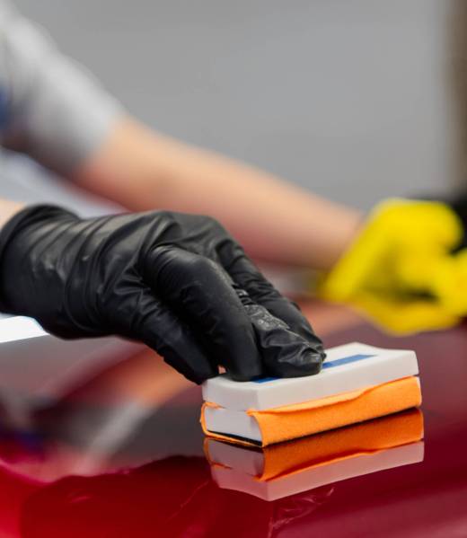 Man worker of car detailing studio applying ceramic coating on car paint with sponge applicator.